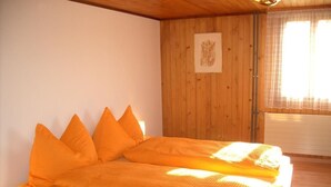 Une pièce aux murs en bois, un lit avec une literie orange et une fenêtre avec des rideaux.