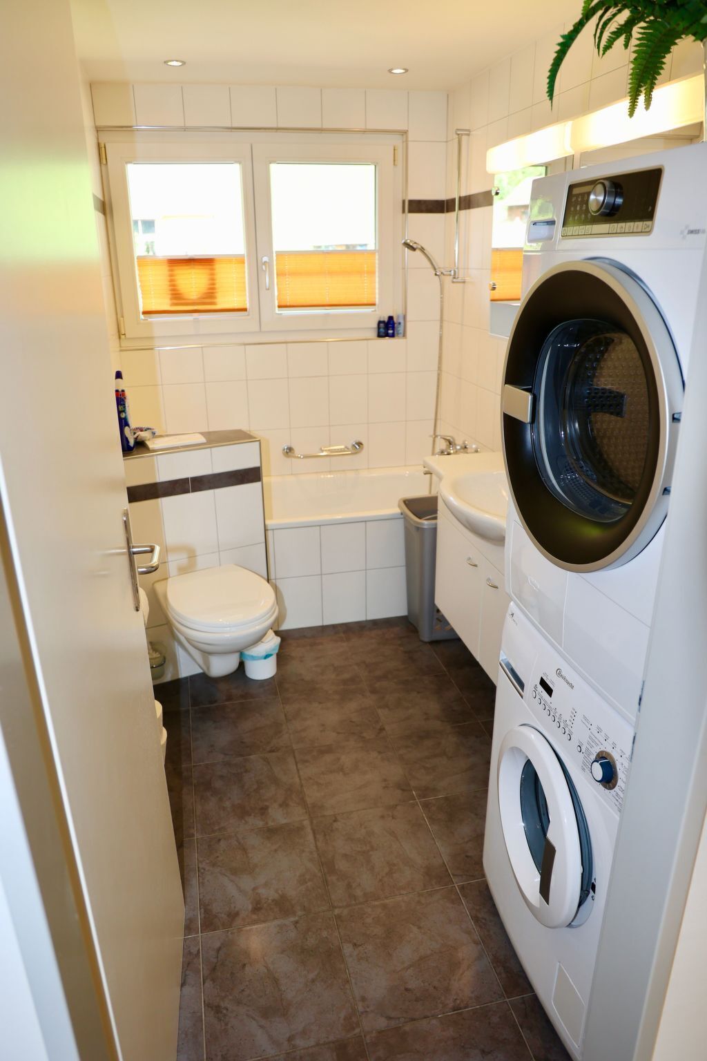 A compact bathroom with a toilet, sink, and a front-loading washing machine.
