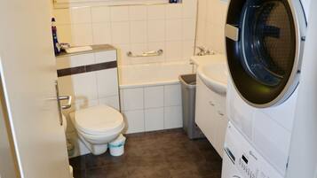 A compact bathroom with a toilet, sink, and a front-loading washing machine.