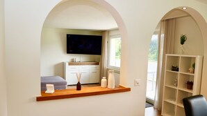 Ein modernes Wohnzimmer mit Fernseher, einer Couch, einem Holzregal mit Dekoration und einem weißen Schrank.
