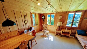 A cozy cabin interior with a wooden dining table, chairs, a rocking chair, a sofa, a lamp, and a clock on the wall. - FeWo Südhang by Interhome (Rüschegg Heubach)