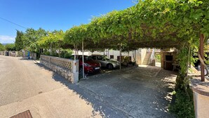 Zona de pàrquing coberta amb una paret de pedra i un cotxe vermell aparcat sota una pérgola coberta de vidre.