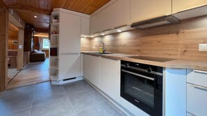 Eine moderne Küche mit Holzschränken, einem eingebauten Backofen und einem gefliesten Boden.