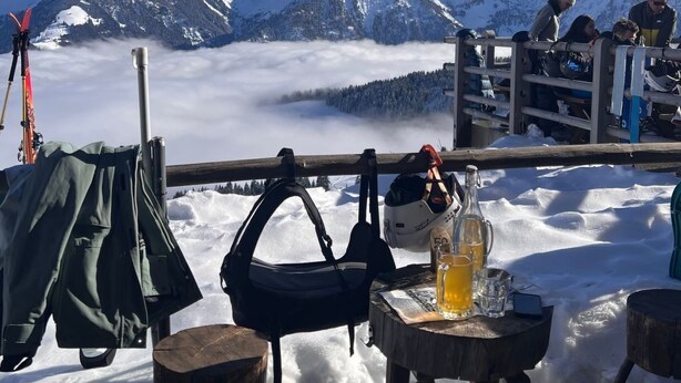 Ein verschneiter Bergblick mit gedecktem Tisch, Ski-Ausrüstung und einer Bierflasche.