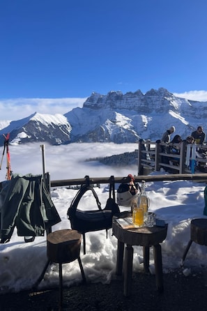 A snowy mountain view with a table set up for a meal, ski equipment, and a bottle of beer. - Apartment  by Interhome (Morgins)
