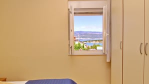 A bedroom with a bed, a window with an open view of a landscape, and wooden flooring.