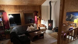 A cozy living room with a fireplace, wooden walls, a sofa, and a chair.