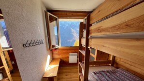A compact, wooden cabin with bunk beds, a small table, and a window offering a mountain view.
