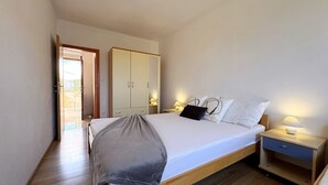 Un dormitorio con cama, mesitas de noche, armario y puerta que da a un balcón.
