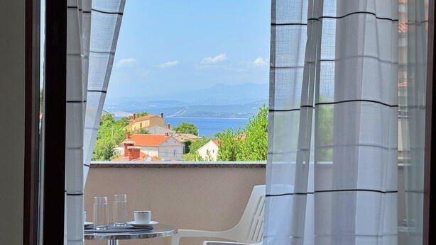 Un balcón con mesa y sillas, con vistas a la costa, casas y montañas.