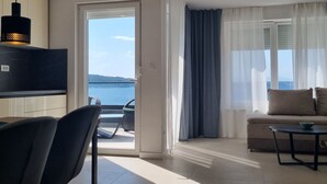 Ein modernes Wohnzimmer mit einer Couch, einem Essbereich mit Stühlen, einem Fernseher und Meerblick durch ein großes Fenster.