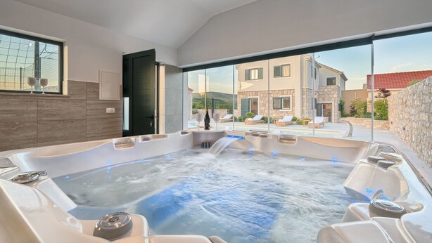 Un área de spa moderna con un jacuzzi, asientos y vistas a un edificio de piedra.