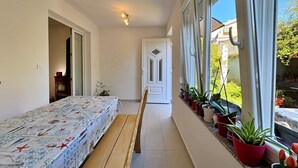 Un pasillo estrecho con una cama a la izquierda, una puerta al final y plantas en macetas a lo largo de la pared derecha.