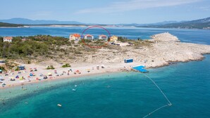 Eine Vogelperspektive einer Küstenlandschaft mit Strand, einer felsigen Halbinsel mit Gebäuden und klarem, blauem Wasser.