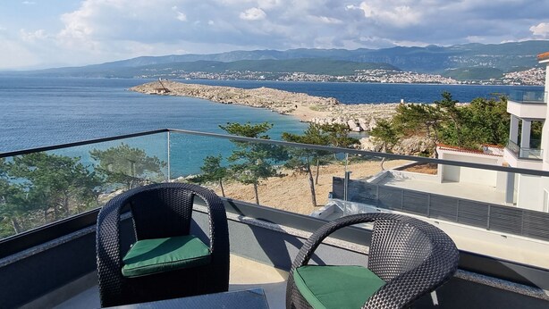 Ein Balkon mit Korbstühlen und Blick auf das Meer und eine felsige Küste.