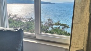 Ein Zimmer mit großem Fenster, das auf ein Gewässer und eine ferne Bergkette blickt.