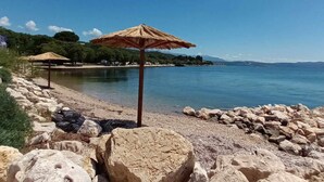 En stenstrand med ett parasoll av halmtak och fri utsikt över vattnet och de avlägsna bergen.