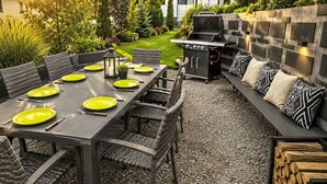 Un área de comedor al aire libre con una mesa larga, sillas y un banco integrado con cojines.
