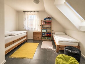 Ein gemütliches Schlafzimmer mit zwei Betten, einem Bücherregal, einem Fenster mit Vorhängen und einem Dachfenster.