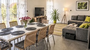 Una sala moderna con un sofá gris, una mesa de comedor con sillas, un televisor y una planta en maceta.