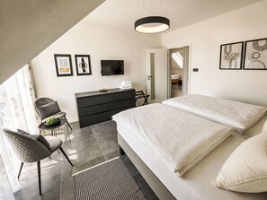 A modern bedroom with a large bed, a dresser, a TV, and artwork on the walls. - Chalet Houbovy vrch by Interhome (Horni Plana)