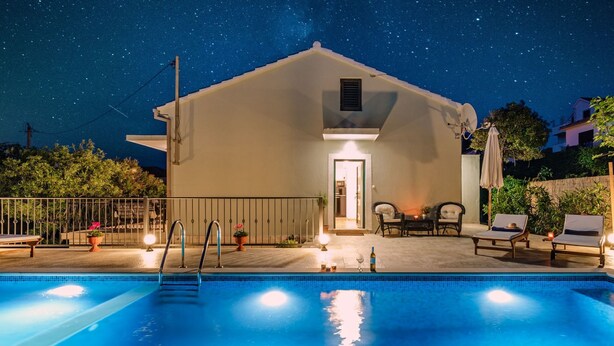 A swimming pool with a metal ladder, a small patio with two chairs and a table, and a building with a door and a satellite dish. - Vacation home Josipa by Interhome (Brač/Supetar)