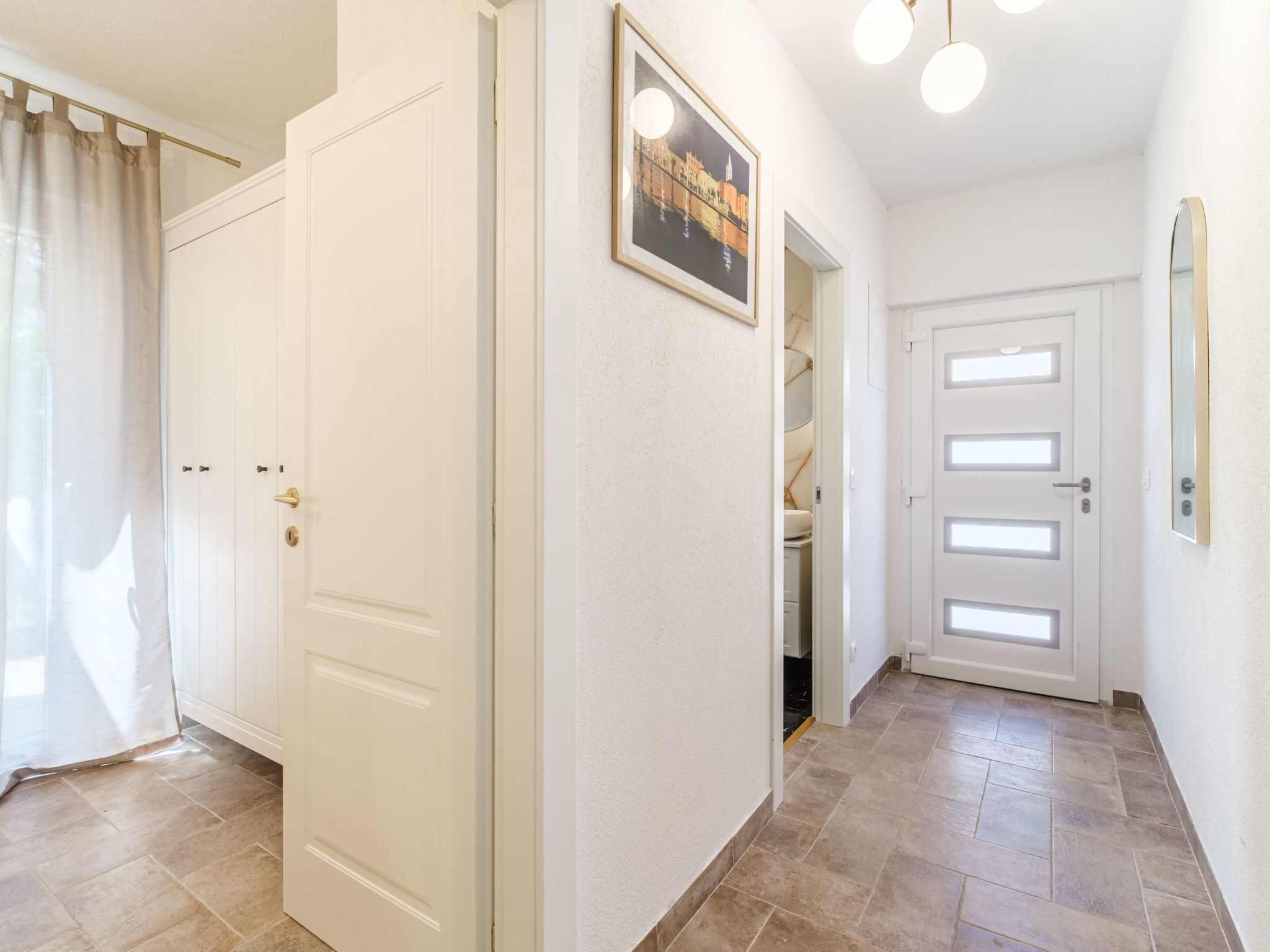 A hallway with a white door, a framed picture on the wall, and a tiled floor.
