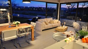 Cozinha moderna com área de jantar, janelas amplas e vista da cidade ao entardecer.