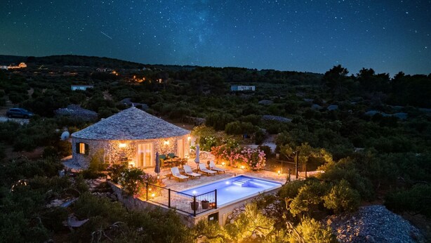 Una casa de piedra con piscina, rodeada de exuberante vegetación y un cielo estrellado.