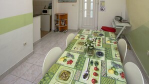 Een eethoek met een tafel voor vier personen, een keuken op de achtergrond en een deur met een bordje.