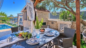 An outdoor patio with a dining table set for two, surrounded by wicker chairs, a stone wall, and a view of a swimming pool. - Villa Antea by Interhome (Kaštel Sućurac)
