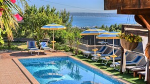 A swimming pool with lounge chairs and umbrellas, surrounded by greenery and a view of the sea. - Villa Antea by Interhome (Kaštel Sućurac)
