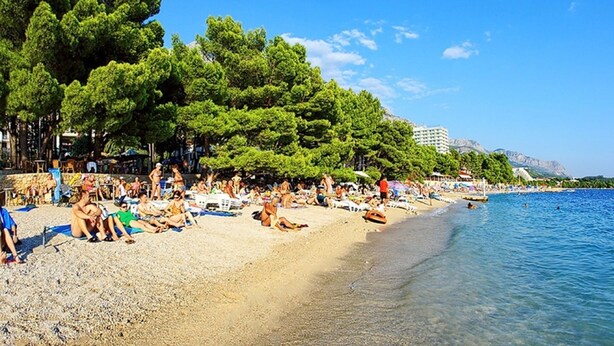 A beach with people sunbathing and swimming, surrounded by trees and a clear blue sky. - Villa Antea by Interhome (Kaštel Sućurac)