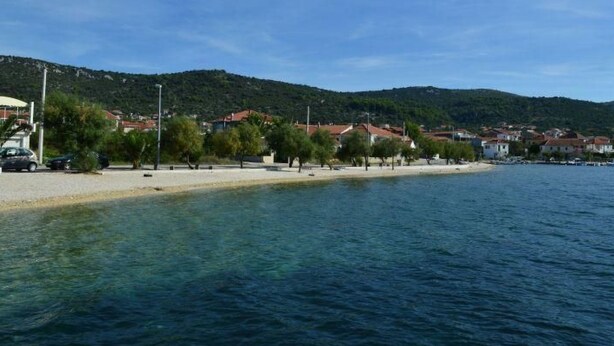 Eine Küstenstadt mit Sandstrand, klarem blauen Wasser und Häusern mit roten Dächern.