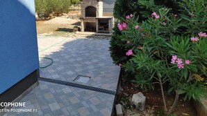 Ein Innenhof mit einem gemauerten Außenofen, einer gefliesten Terrasse und einem Garten mit rosa blühenden Pflanzen.