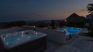Ein Poolbereich auf dem Dach mit Whirlpool und Schwimmbecken, umgeben von Wohngebäuden und Blick auf die Stadt bei Dämmerung.