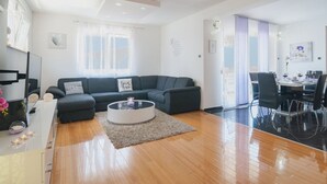 Ein modernes Wohnzimmer mit einem dunkelgrauen Ecksofa, einem runden Couchtisch und einem Essbereich mit einem Glastisch und Stühlen.