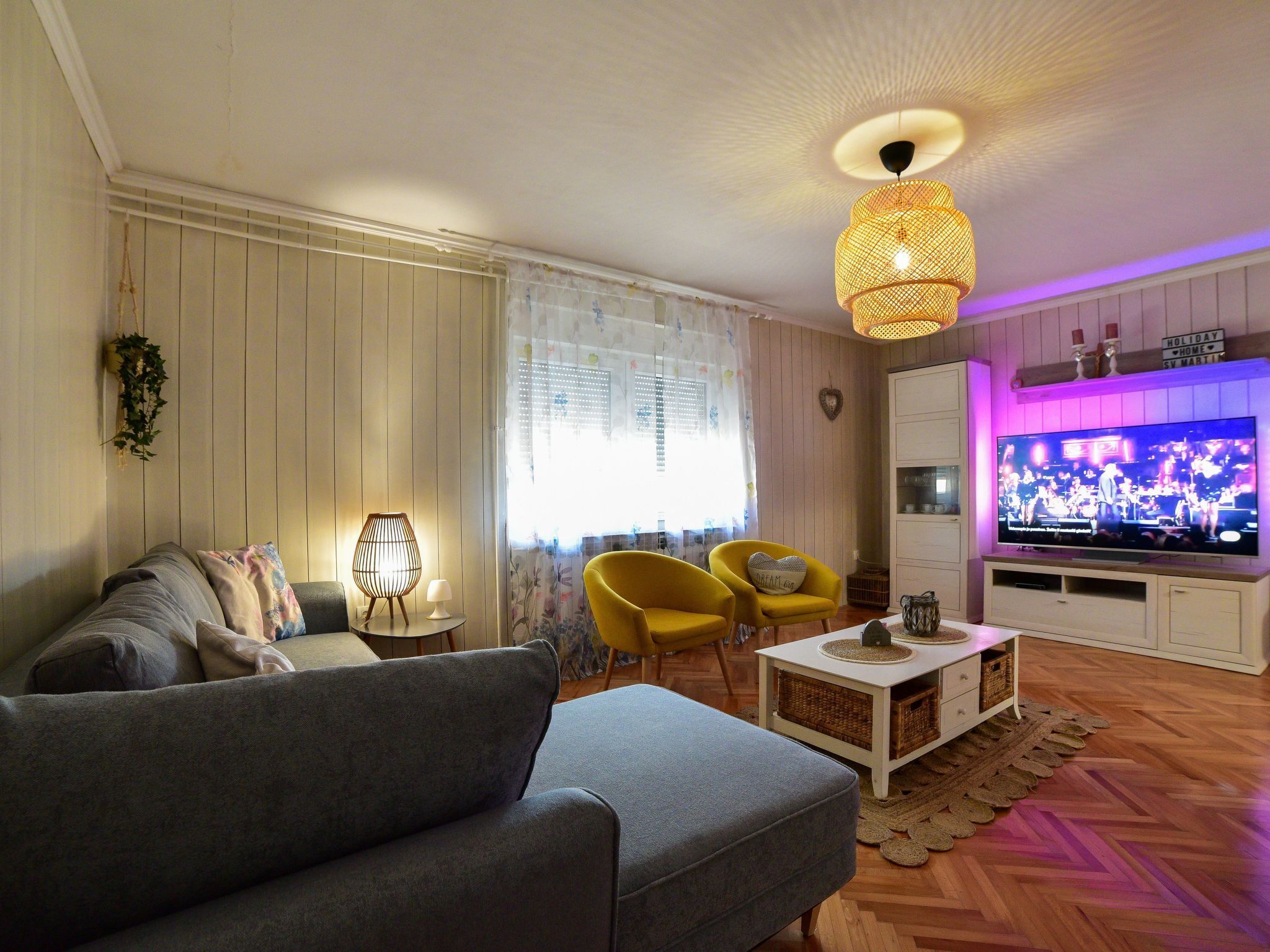 Un salon avec un canapé, deux fauteuils jaunes, un téléviseur et un luminaire suspendu.
