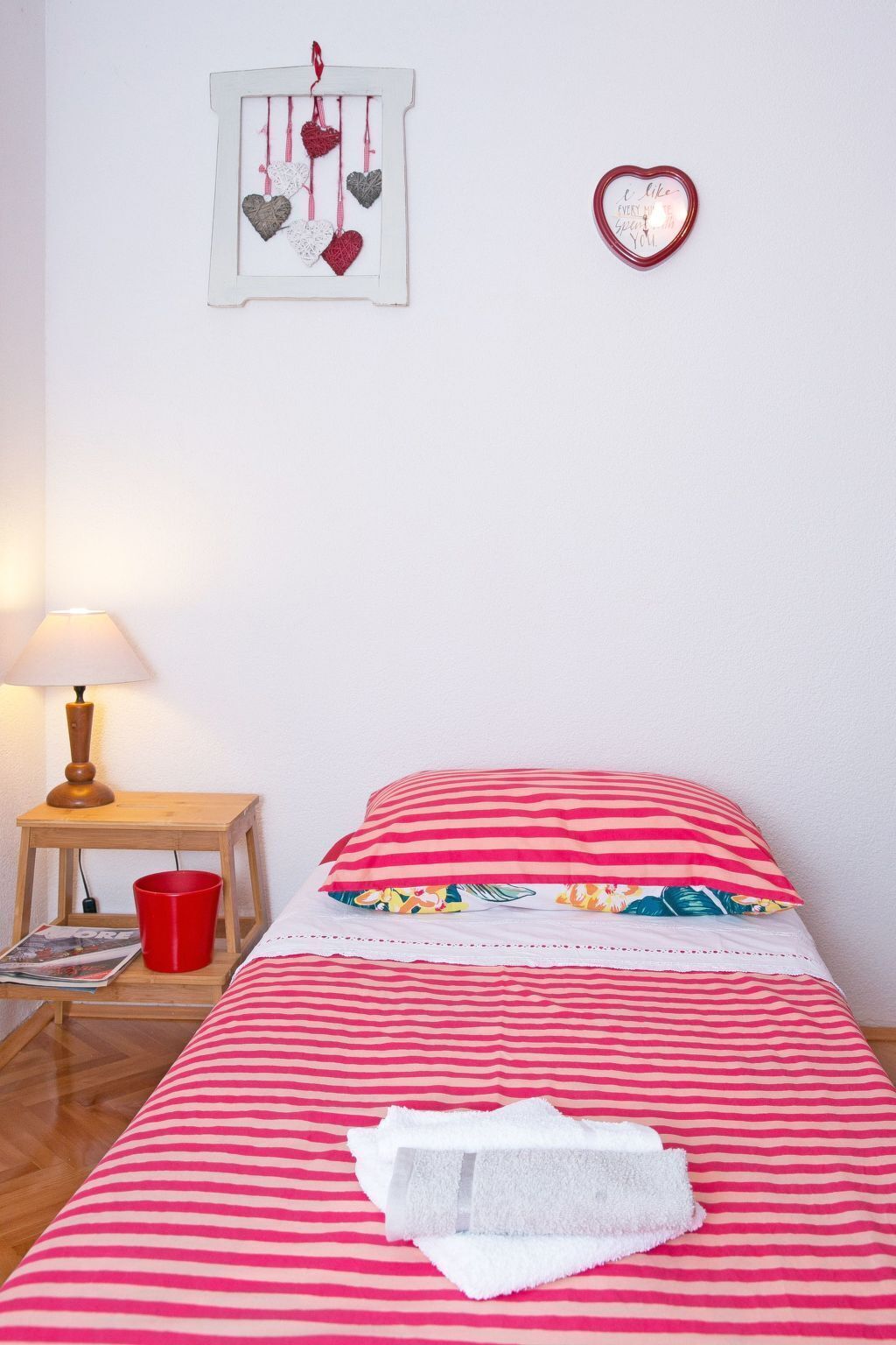A bedroom with a bed, a nightstand, a lamp, and heart-shaped decorations on the wall.