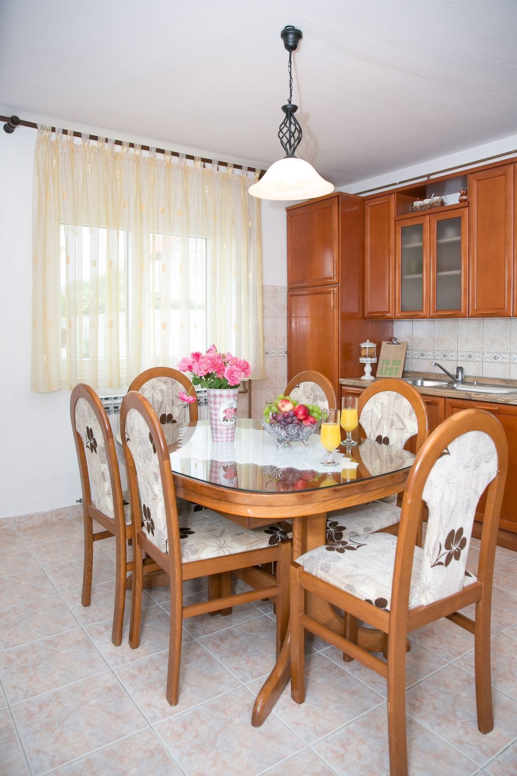 A dining area with a round table, six chairs, a vase of flowers, and a fruit bowl.