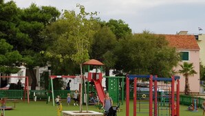 A playground with various play structures, including a slide and climbing frames, surrounded by greenery and buildings. - Strandappartement Ana mit Meerblick, Garten, Grillplatz by Interhome (Dragišina)