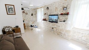 Ein Wohnzimmer mit Steinsturz, einem an der Wand befestigten Fernseher, einem Essbereich mit Tisch und Stühlen sowie einem Sofa.