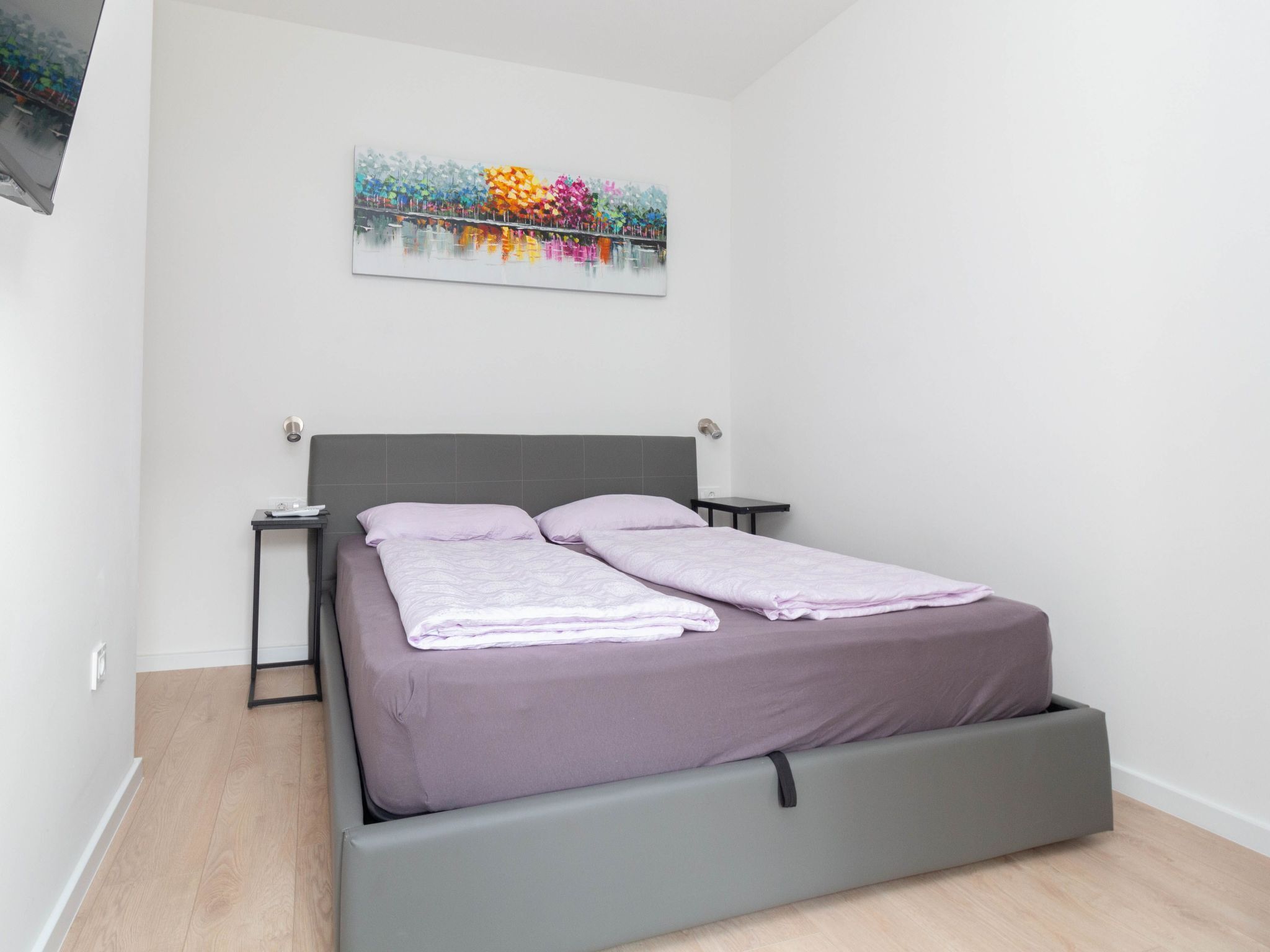Un dormitorio moderno con una cama, dos mesitas de noche y un cuadro colgado en la pared.