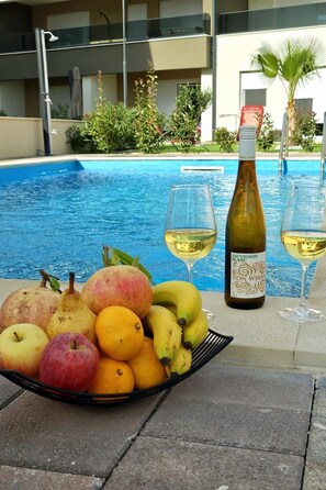 Ein Tisch am Pool mit einer Weinflasche, zwei Gläsern und einem Obstkorb.