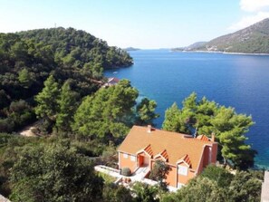 Ein Küstenanwesen mit einem rotdachigen Haus, umgeben von üppiger Vegetation und Blick auf das Meer.