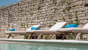 Zona de piscina amb gandules i una paret de pedra.