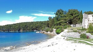 Una platja costanera amb mar blau clar, pendent rocos i un edifici de pedra històric.