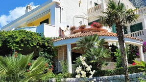 A white building with a curved roof and a garden with various plants and flowers. - Villa Margitta mit Pool, Tennisplatz und Meerblick by Interhome (Drašnice)