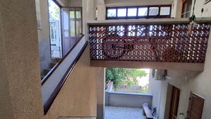 Un intérieur à plusieurs niveaux avec un escalier, un balcon doté d’une balustrade ornée, et une cour dallée.