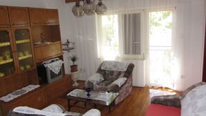 Un salon avec des meubles en bois, un canapé, un fauteuil, une table et une fenêtre avec des rideaux.